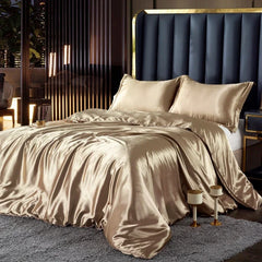 Beige satin bedding set on a bed with a dark blue upholstered headboard.