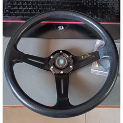 Black steering wheel on a desk with a keyboard in the background